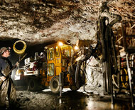 A miner stands off to the side as a machine works in an underground silver mine.