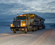 An ore haulage truck travels along a dirt road at dusk.