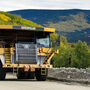 Mining truck hauls gold ore against a backdrop of yellow fall foliage in Alaska.
