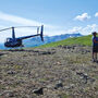 Helicopter and pilot on a ridge at Coal Creek during a summer day in Alaska.