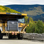 Mining truck hauls gold ore against a backdrop of yellow fall foliage in Alaska.