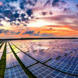 Colorful sunset reflects off photovoltaic panels at a large solar power plant.