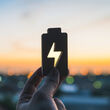 A battery cutout with a voltage symbol being held up to an orange sunset.