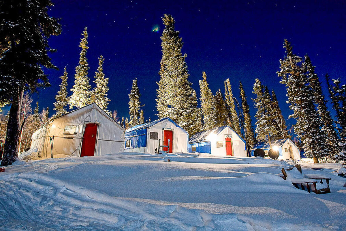 Camp lights illuminate the cabins and snow at a mineral exploration camp.