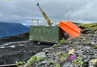 Violet flowers grow out of rocks in front of drill testing for gold at Cassiar.
