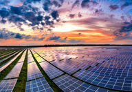 Colorful sunset reflects off photovoltaic panels at a large solar power plant.