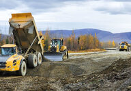 Articulating trucks, dozer, and compactor upgrade road during fall in Alaska.