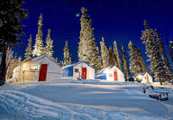 Camp lights illuminate the cabins and snow at a mineral exploration camp.