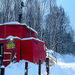 Red drill rig tests for gold in a birch tree forest during the winter in Alaska.