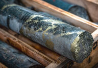 Dark grey drill core with bands of metallic gold-colored copper mineralization.