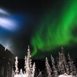 A band of green aurora behind a drill testing for gold during winter in Alaska.