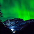 Mountain at Kensington mine silhouetted by brilliant green aurora display.