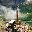 Looking down on a drill rig perched above clouds on the side of a mountain.