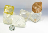 A collection of large yellow, white, and brown rough diamonds with one cut gem.