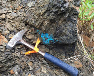 A rock hammer lies next to copper-rich blue mineralization at Galore Creek, BC.