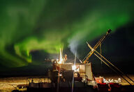 Band of green aurora behind a drill testing for gold at night at Goose.