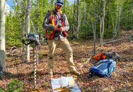 Geologist with hand augur drill collects soil samples from the forest floor.