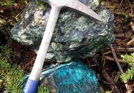 Rock hammer next to samples stained blue with copper mineralization in BC.