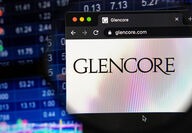 Stock market ticker board backdrops a smartphone with Glencore logo.