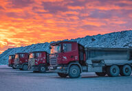 A colorful sunset illuminates a line of underground mining trucks.