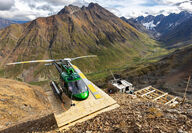 A green helicopter landed in front of orange-stained mountains at Rogue.