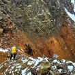 A geologist investigates a band of oxidized mineralization on a mountain ridge.