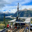A drill testing for copper and gold overlooks a river and mountains in BC.