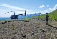 Helicopter and pilot on a ridge at Coal Creek during a summer day in Alaska.