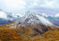 Snow-dusted mountains rise above orange landscape during fall in Alaska.