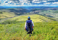 Geologist stands on a green hill overlooking the breathtaking Yukon scenery.