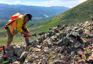 Geologist using a hammer to collect samples from a rock outcrop in Alaska.