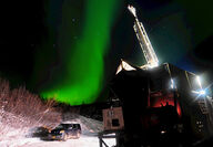 A green streak of the aurora over a drill rig set up in winter.
