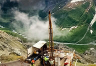 Looking down on a drill rig perched above clouds on the side of a mountain.