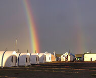 Rainbow touches down behind row of white tents in Nunavut, Canada.