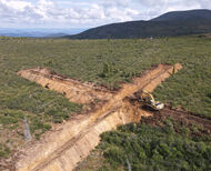A cross shaped trench with an excavator in the middle of the Yukon wilderness.