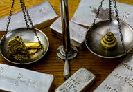 Silver bars and a balance scale with gold on one side and weights on the other.