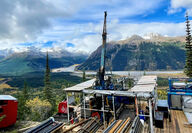 A drill testing for copper and gold overlooks a river and mountains in BC.