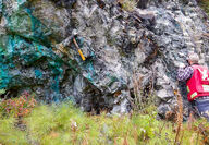 A geologist on an outcrop stained green with copper in Northern BC, Canada.