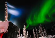 A band of green aurora over a drill testing for gold on an Alaska winter night.