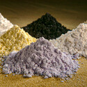 Piles of white, grey, black, and yellow rare earth oxide powders.