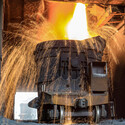 A shower of sparks arcs away as molten steel pours into a large industrial vat.