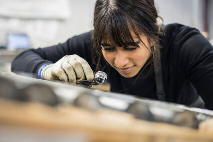 Female technician takes closer look at gold in core with a geologist loupe.