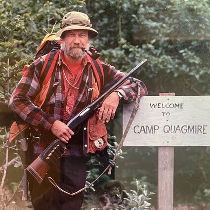 Longtime Alaska geologist Bill Ellis beside a Camp Quagmire sign.