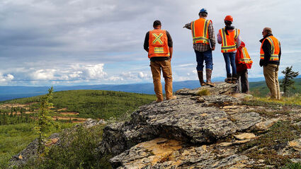 Geologists, investors, and executives standing on a rock outcrop at Manh Choh.
