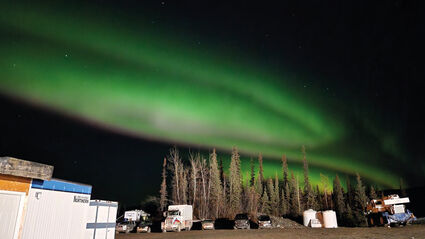 The northern lights above a brightly lit AurMac camp.