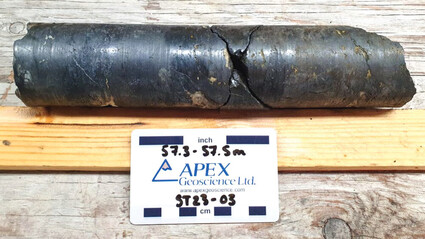 An 8-inch section of gunmetal-colored drill core that is roughly 50% copper.