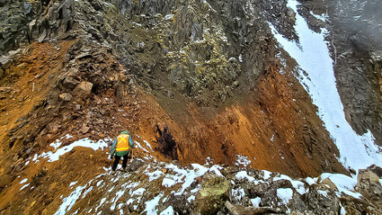 A geologist investigates a band of oxidized mineralization on a mountain ridge.