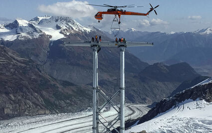 Helicopter positions a part on a powerline above BC glaciers and mountains.