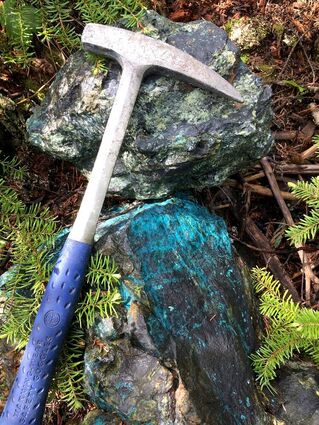 Rock hammer next to samples stained blue with copper mineralization in BC.