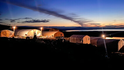 Lights paint large Graphite Creek camp tents with an orange hue during dusk.